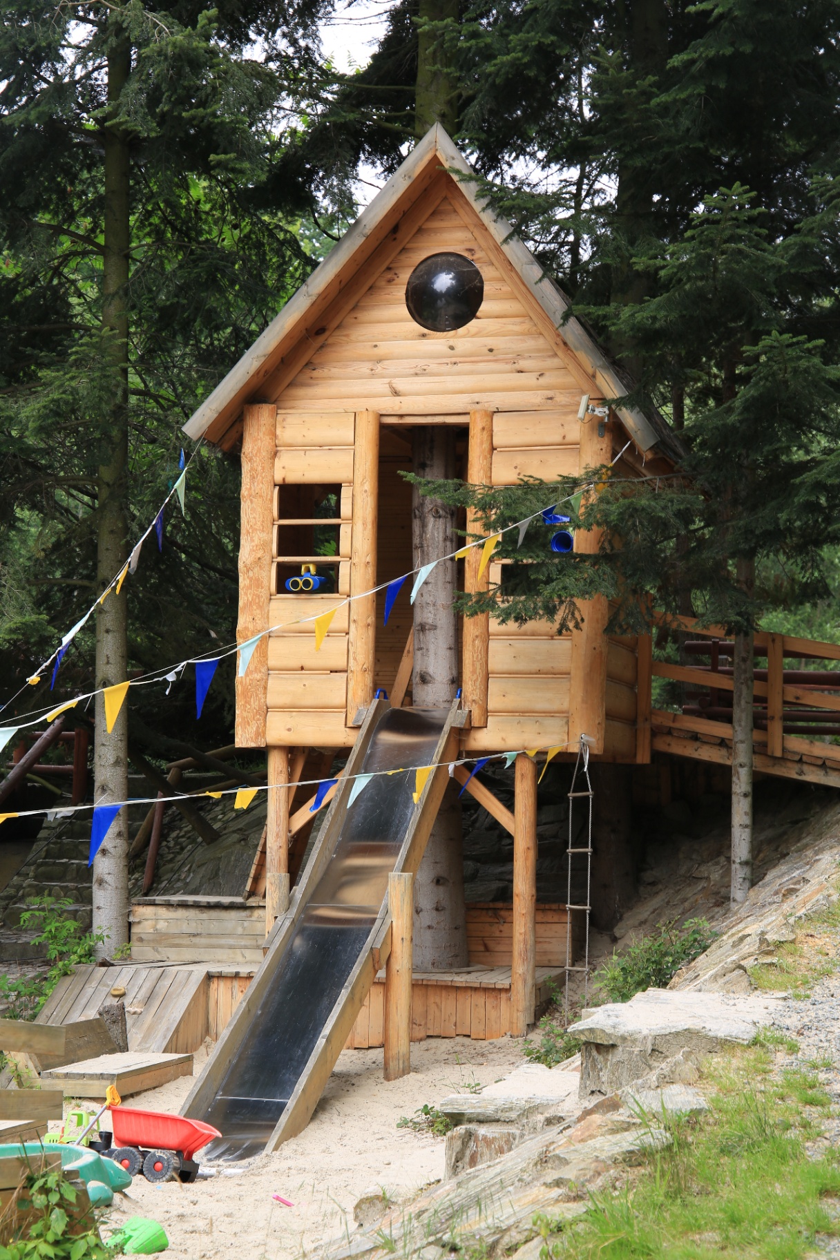 Drewniany domek na drzewie z metalową zjeżdżalnią i piaskownicą